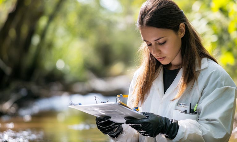 Early-career environmental professional conducting monitoring in a natural environment.